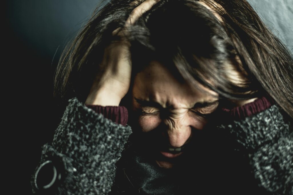 pexels-photo-2128817-2128817 Close-up of a woman in distress with eyes closed and hands in hair, expressing anxiety.